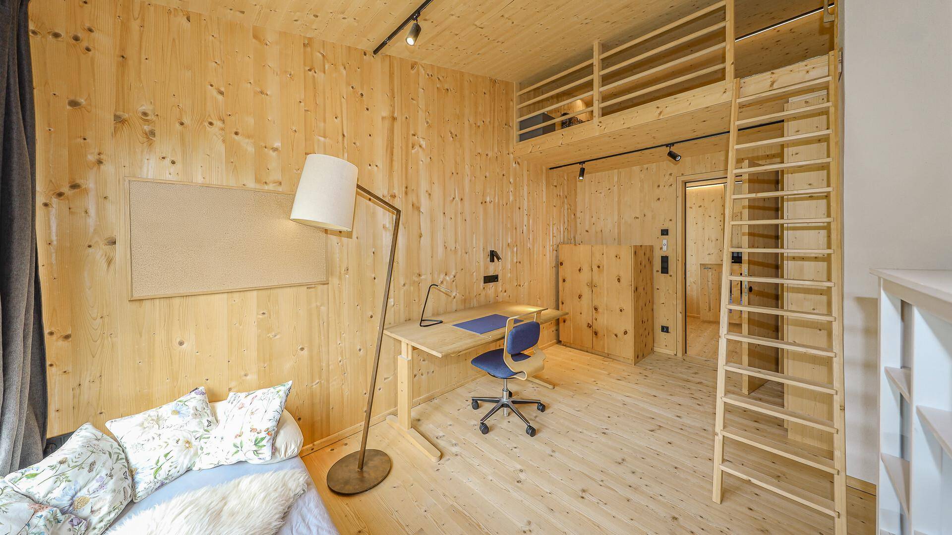 Geräumiges Zimmer mit Holzwänden, Schreibtisch und Hochbett, bietet vielseitige Nutzungsmöglichkeiten.