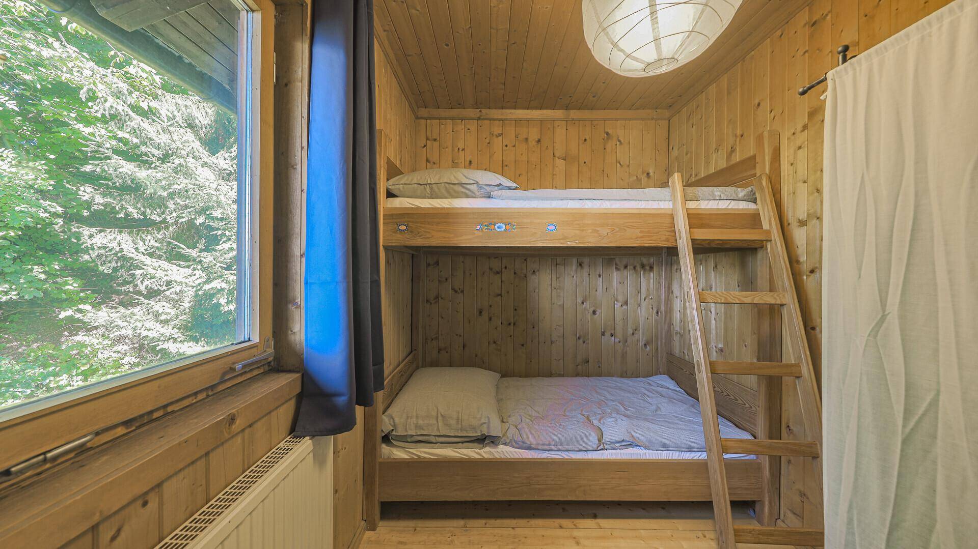 Kinderzimmer mit Etagenbett, Holzwänden und Fenster mit Blick ins Grüne.
