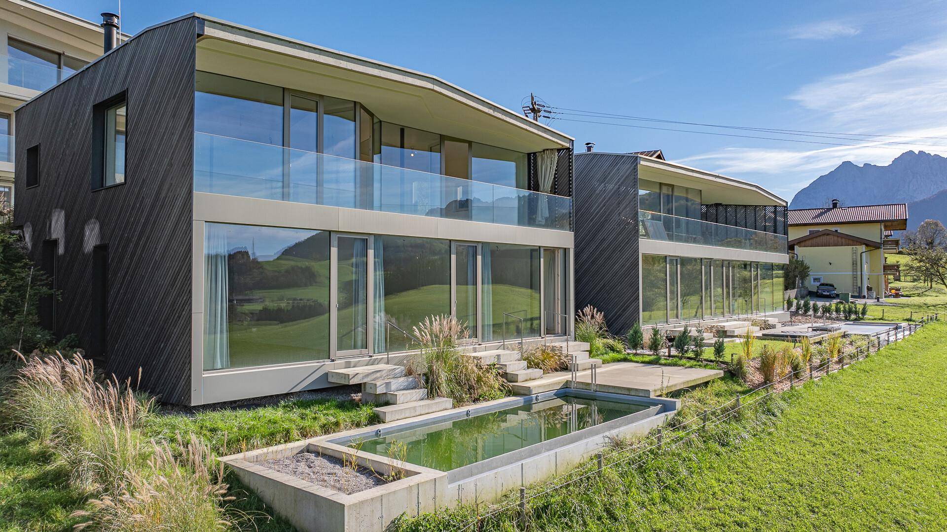 Zwei moderne Gebäude mit Holzfassade, Glasfronten und einem Poolbereich in ländlicher Umgebung.