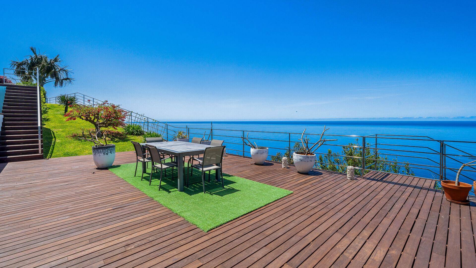 Große Holzterrasse mit Esstisch, weitem Meerblick und direktem Zugang zum Garten.