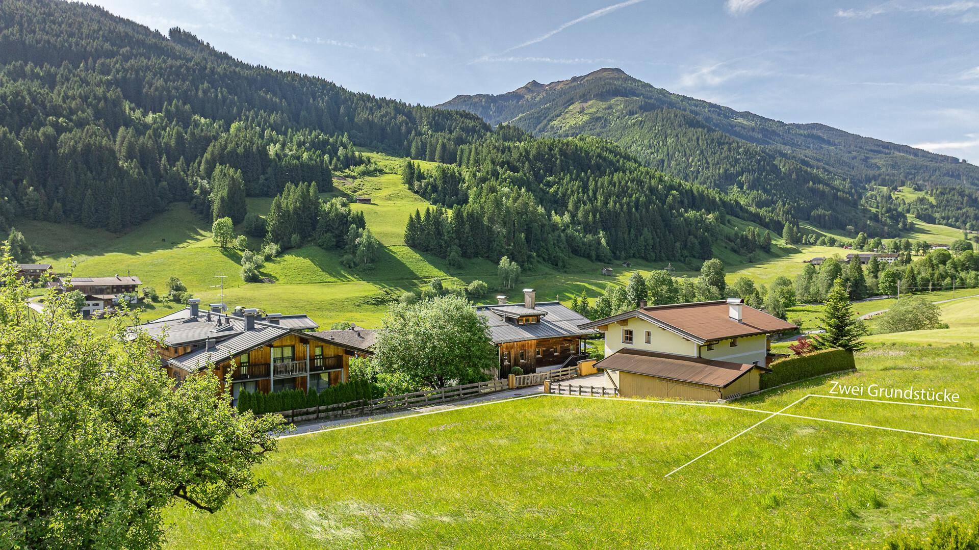 Panoramablick auf ein grünes Tal mit markierten Grundstücken, umgeben von Wäldern und Bergen.