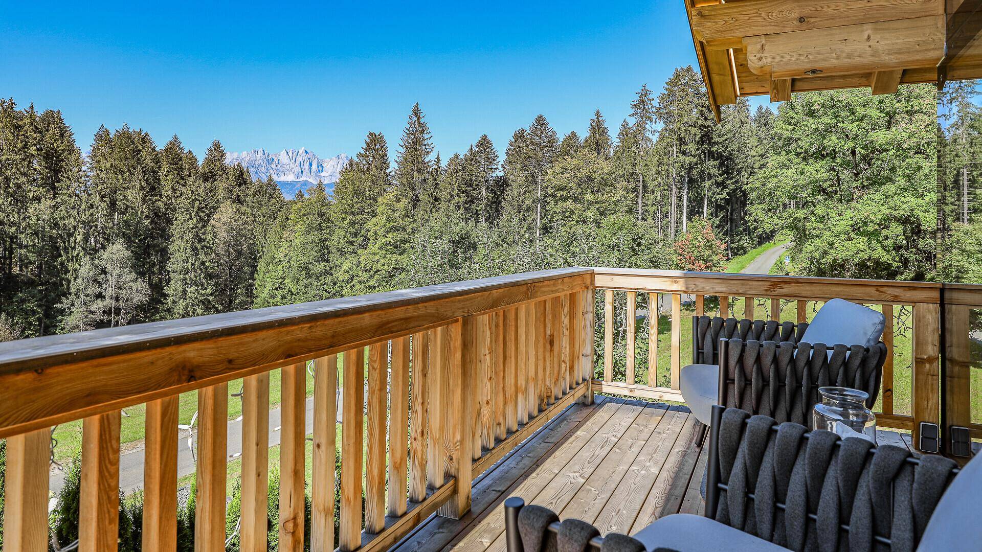 Geräumiger Holzbalkon mit Sitzgelegenheiten und weitem Blick auf die bewaldeten Berge.
