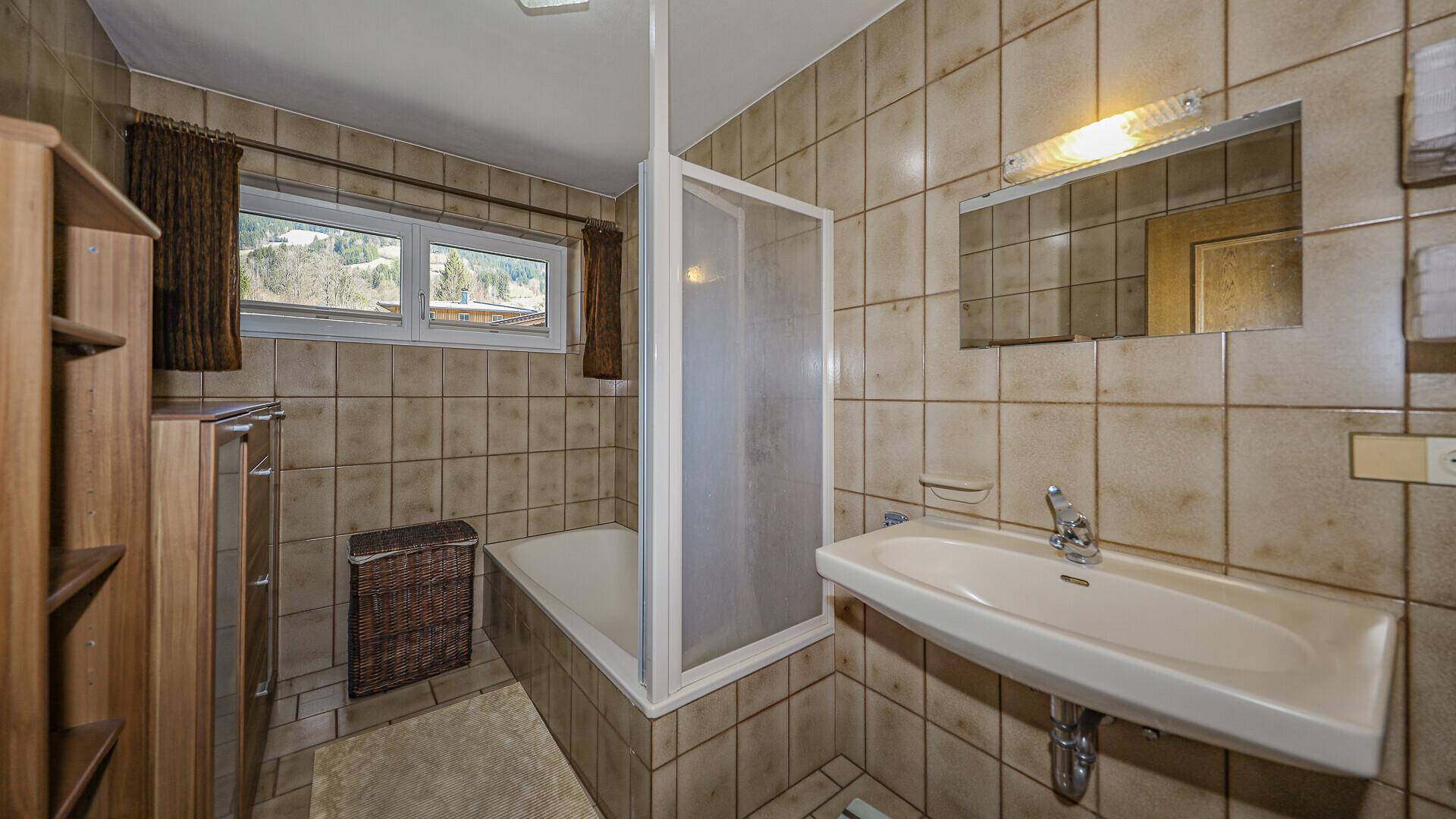 Badezimmer im 80er-Jahre-Stil mit Badewanne, Dusche und Fenster mit Bergblick.