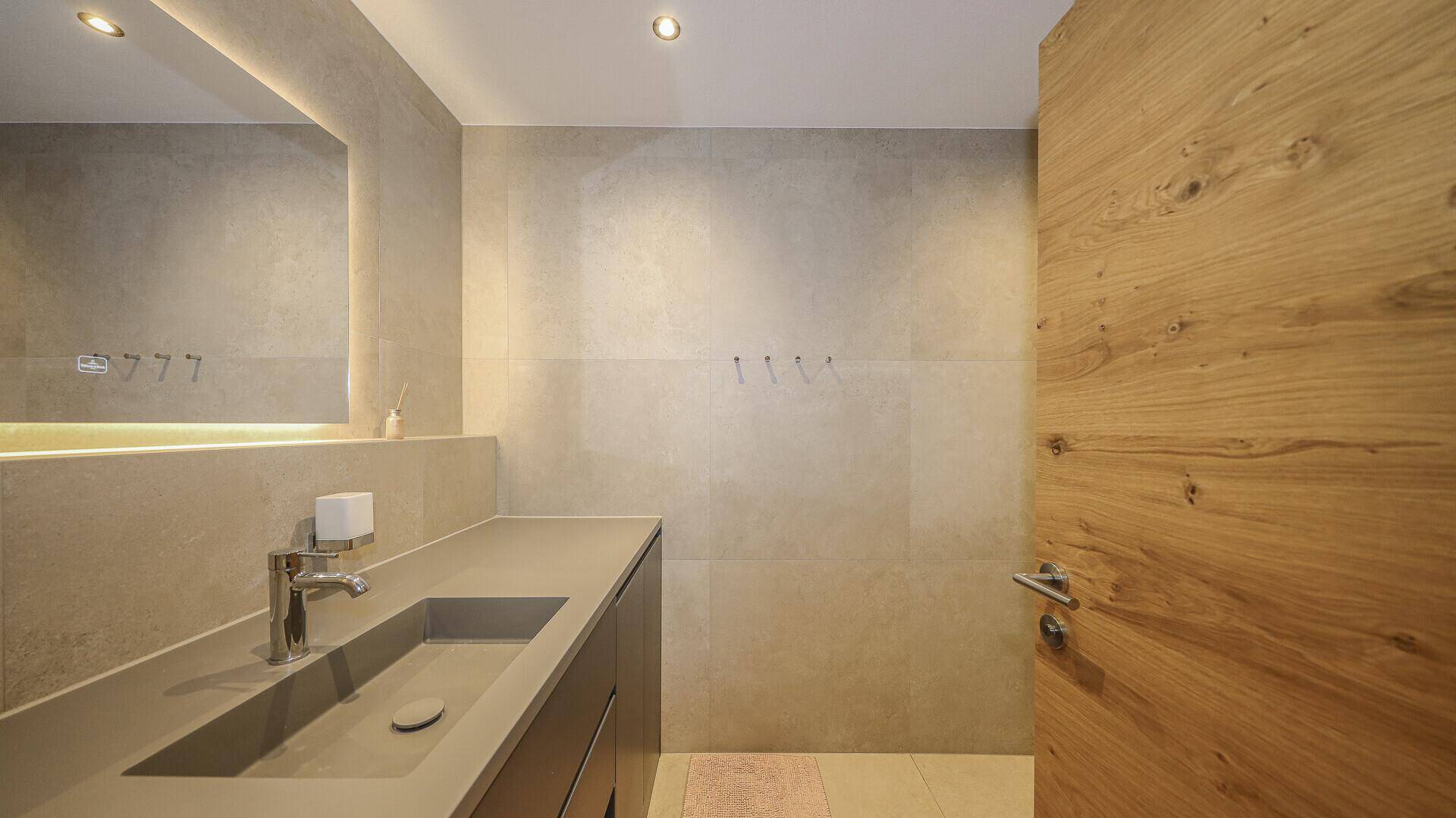 Modernes Badezimmer mit großformatigen Fliesen, Einzelwaschbecken und integriertem Spiegel.