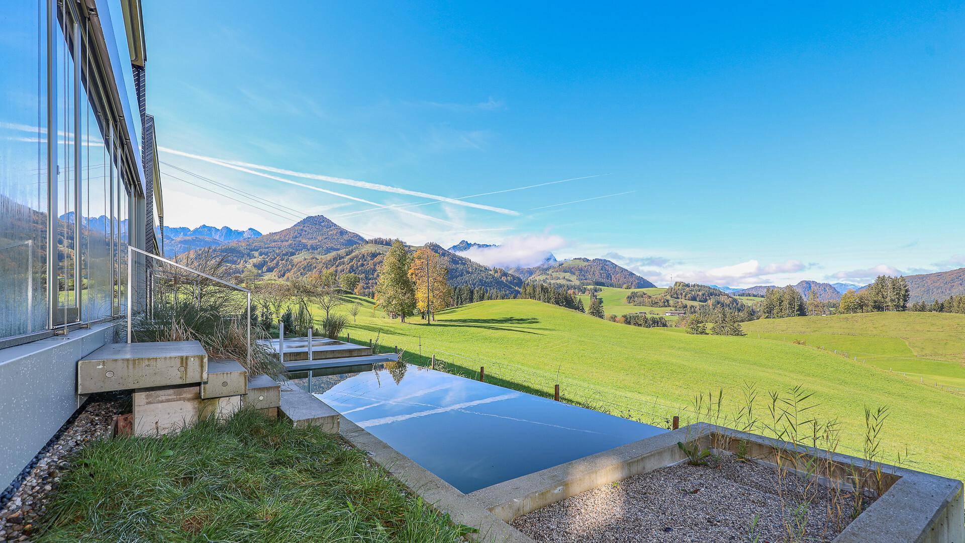 Außenbereich mit Infinity-Pool und weitem Blick auf die grüne Hügellandschaft und Berge.