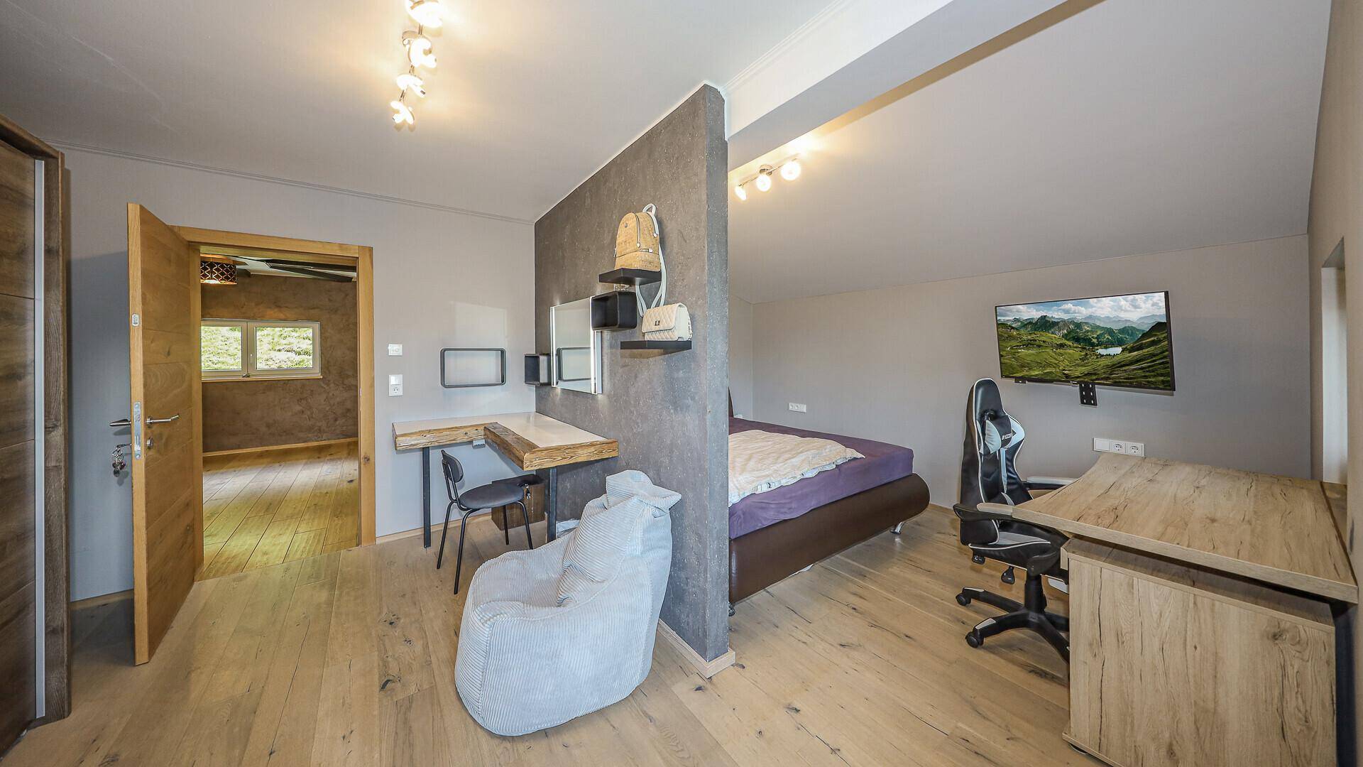Geräumiges Schlafzimmer mit Holzboden, Schreibtisch und separatem Schlafbereich.