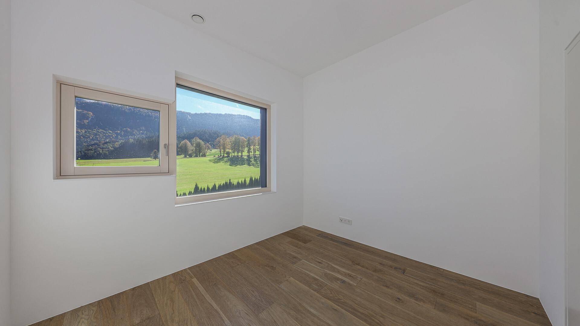 Leeres Schlafzimmer mit Holzboden und Fenstern, die einen weiten Blick auf die Natur ermöglichen.