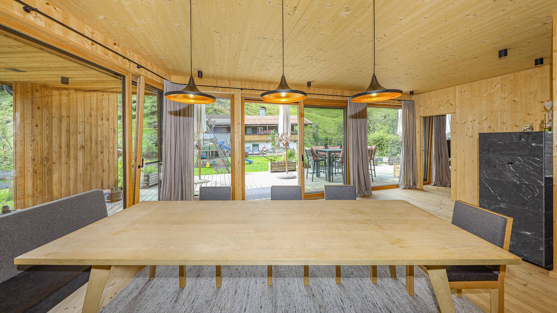 Essbereich mit großem Holztisch und Zugang zur Terrasse, umgeben von Holzwänden und Holzboden.