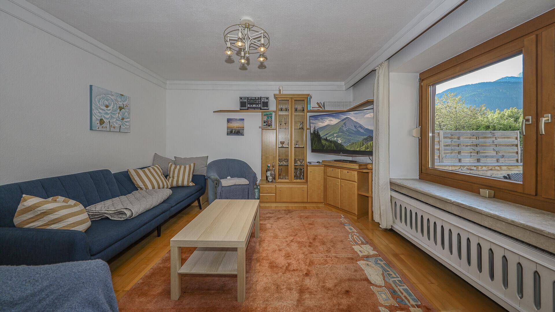 Gemütliches Wohnzimmer im traditionellen Stil mit blauem Sofa, Holzmöbeln und Bergblick.