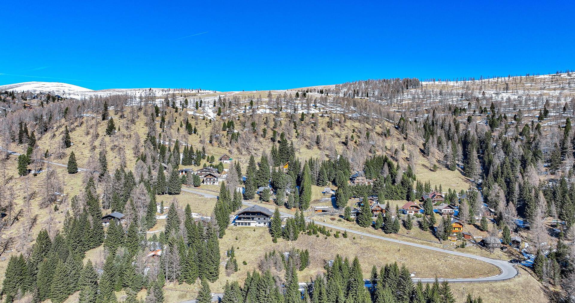 Panoramablick auf eine alpine Landschaft mit verstreuten Häusern und kurvigen Straßen unter blauem Himmel.
