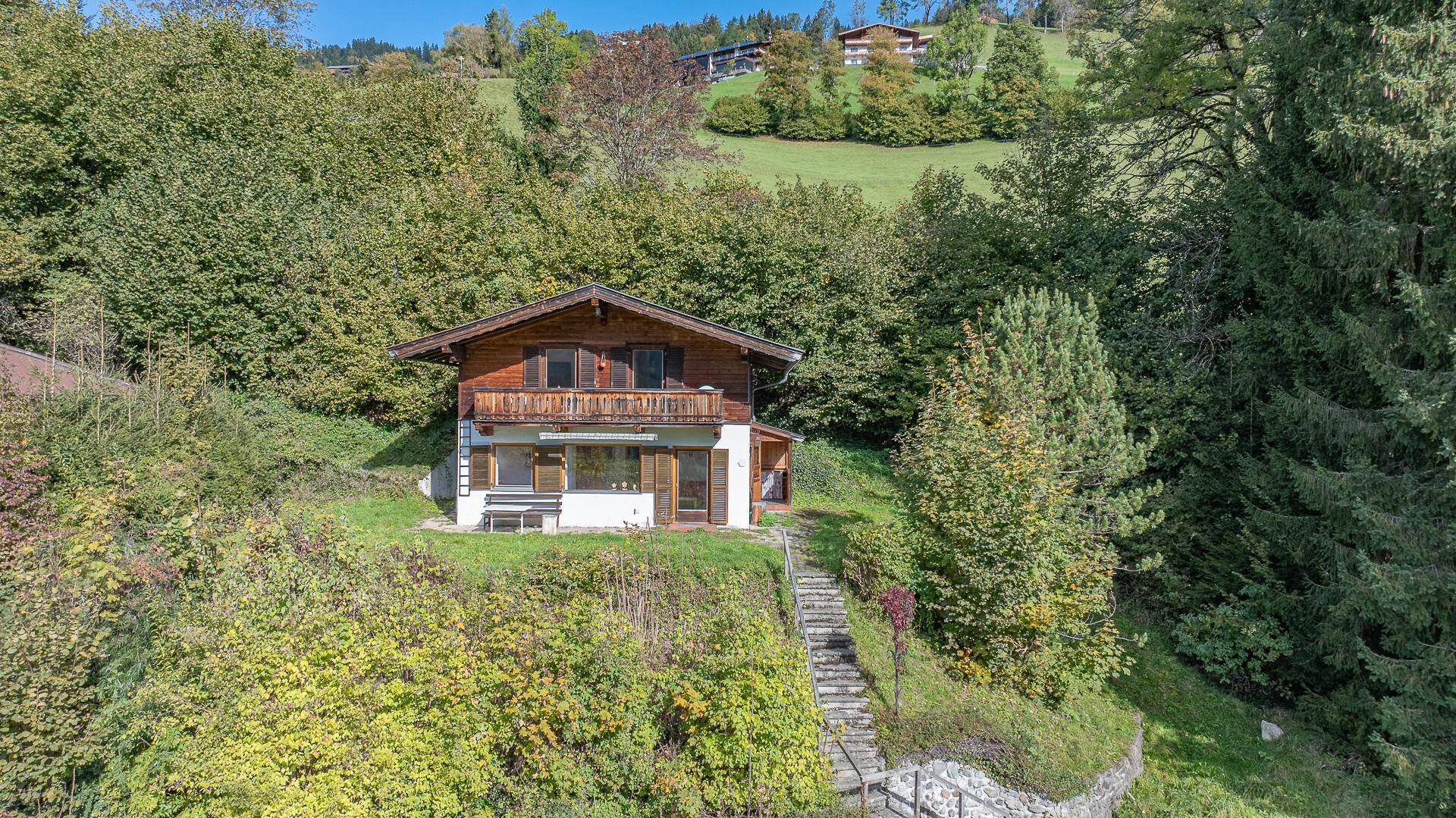 Traditionelles Holzhaus in alpiner Umgebung, umgeben von üppiger Vegetation und Bäumen.