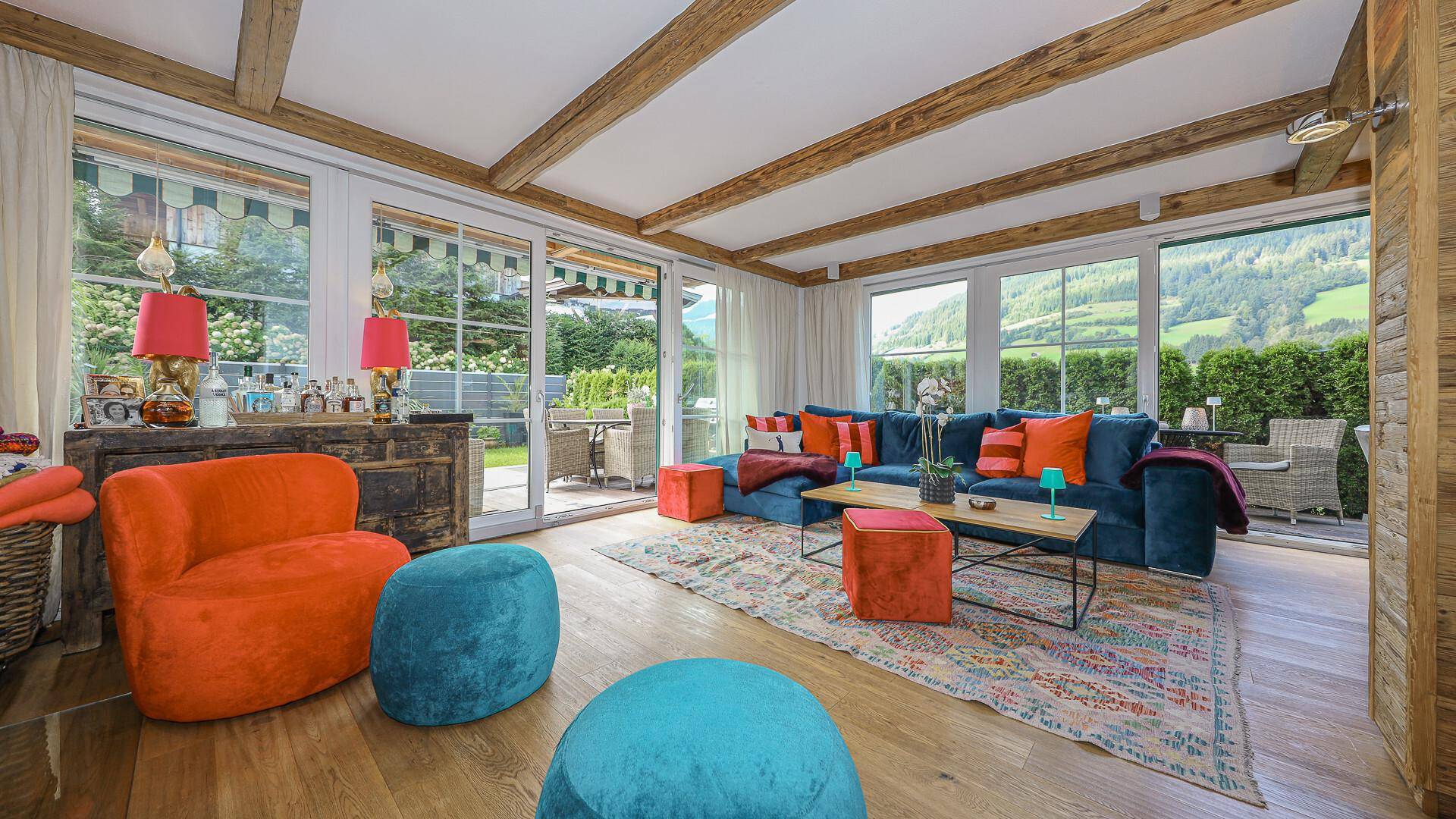 Gemütliches Wohnzimmer mit großen Fenstern, bunten Sitzmöbeln und direktem Zugang zur Terrasse.