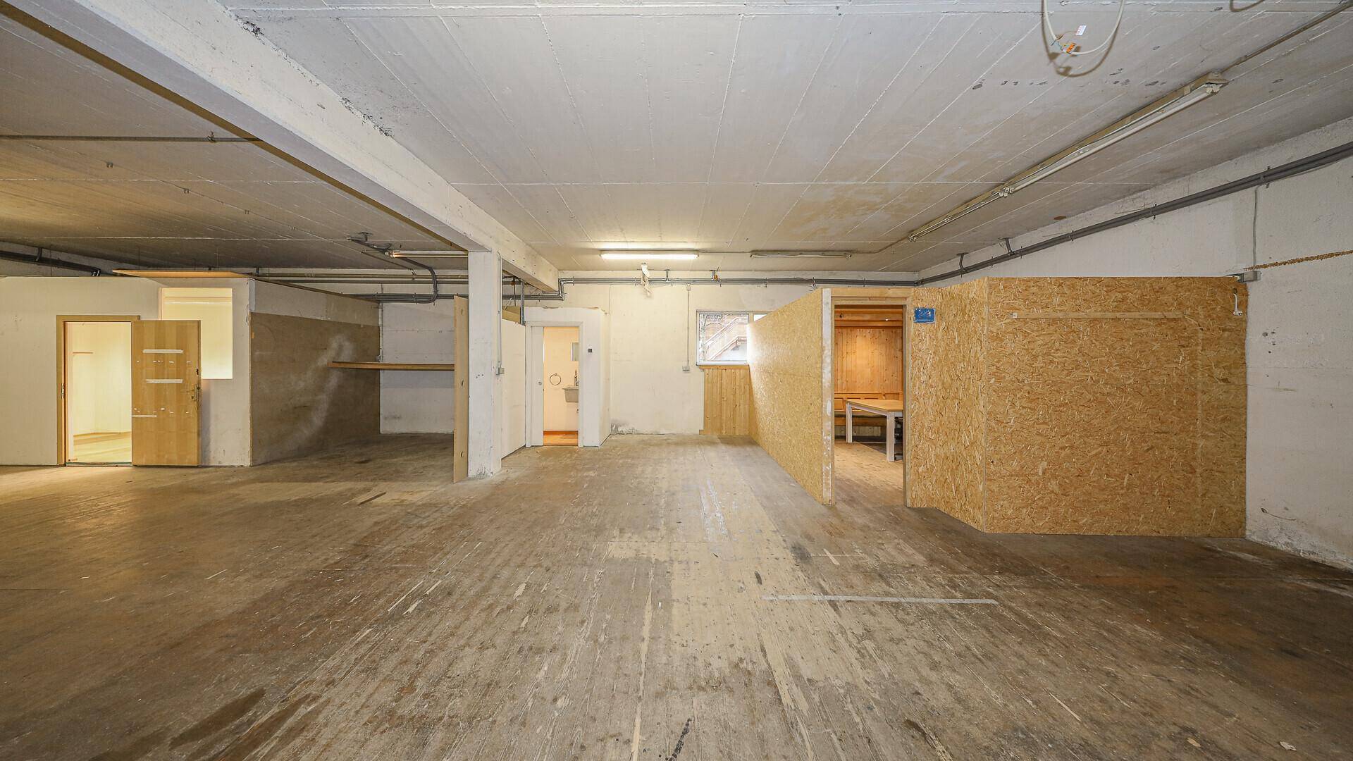 Geräumiger Lagerbereich mit Betonboden, verschiedenen Zugängen und einer abgetrennten Holzwandkonstruktion.