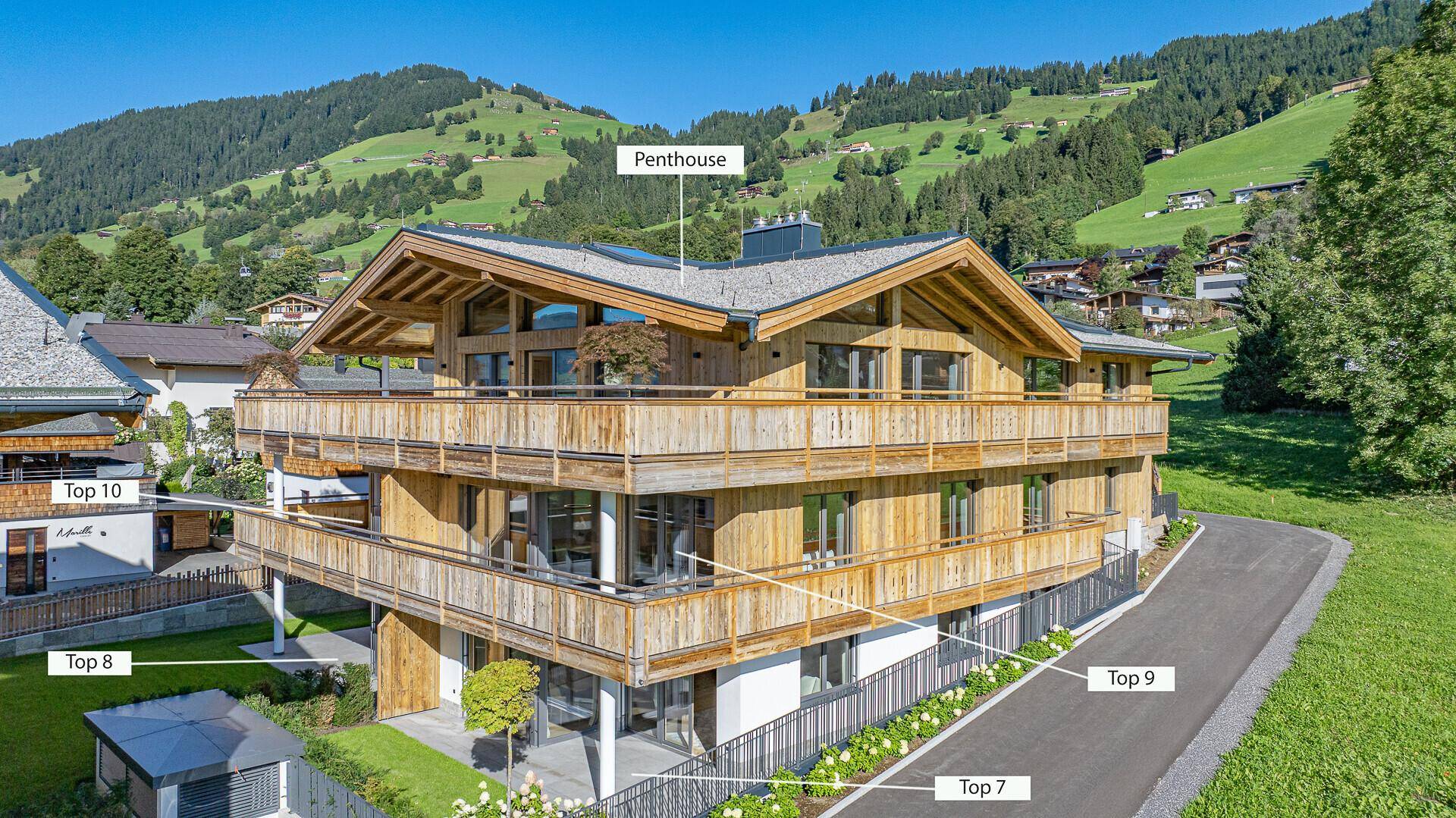 Attraktives Mehrfamilienhaus im alpinen Stil mit Holzbalkonen und Bergblick, bei Tageslicht.
