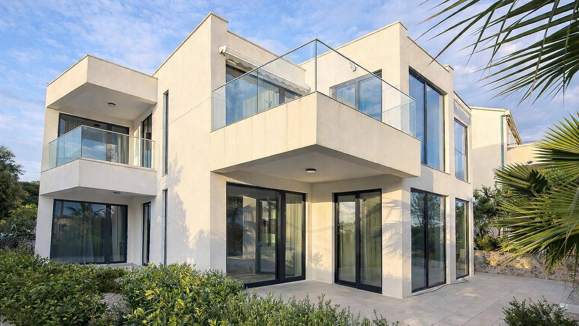 Elegante moderne Villa mit mehreren Balkonen, Glasgeländern und großen Fensterfronten.