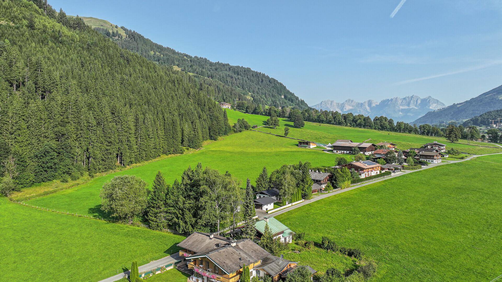 Luftaufnahme des Anwesens in einer weiten grünen Landschaft mit bewaldeten Bergen im Hintergrund.