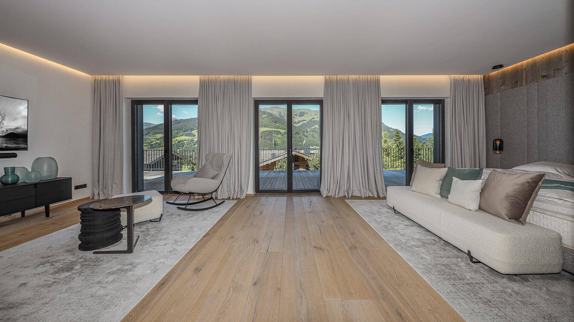 Geräumiges Schlafzimmer mit Holzboden, indirekter Beleuchtung und Zugang zum Balkon mit Bergblick.