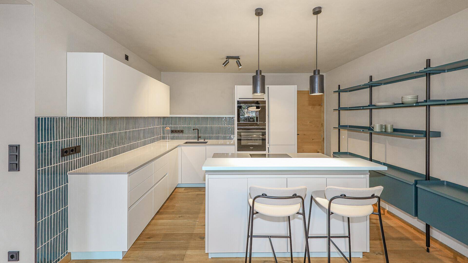 Stilvolle Küche mit weißen Schränken, Kochinsel und blauen Akzenten an der Wand.