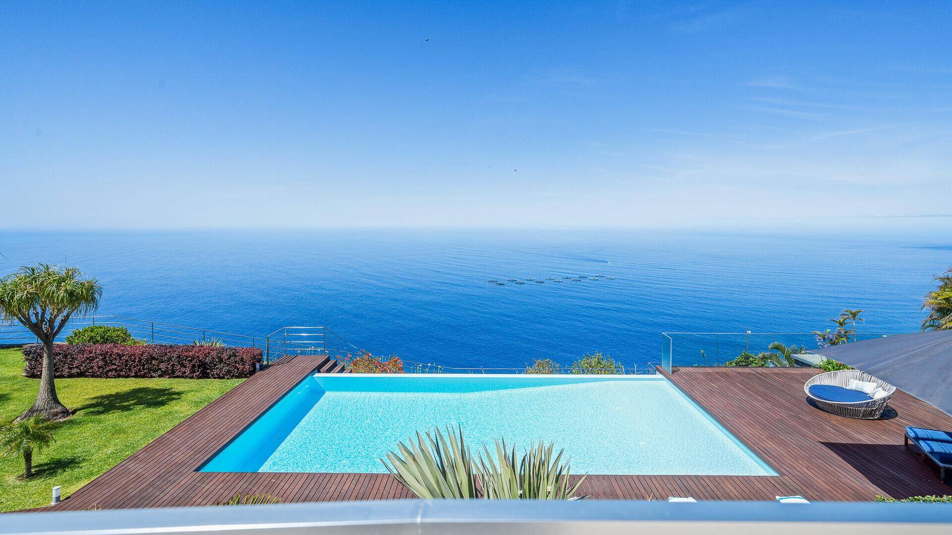 Infinity-Pool mit Holzdeck und Rasenfläche, bietet einen unverbauten Blick auf das weite, blaue Meer.