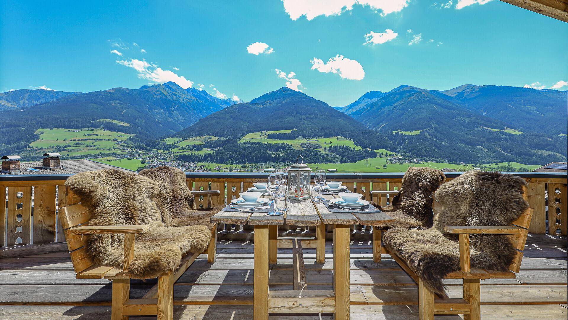 Große Terrasse mit Holztisch und Fellen, ideal für Mahlzeiten im Freien mit Bergblick.