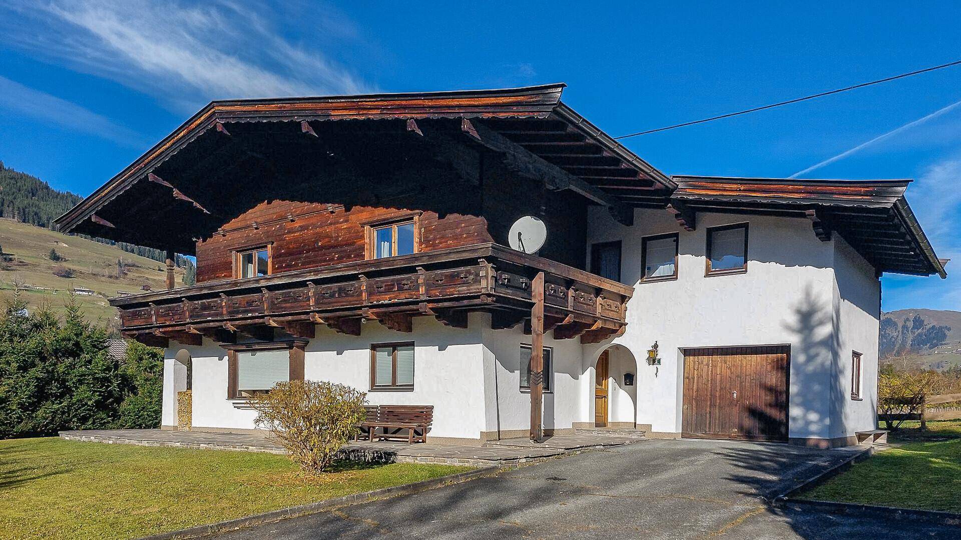 Traditionelles Haus mit weißer Fassade, Holzbalkonen und Satteldach in alpiner Umgebung.
