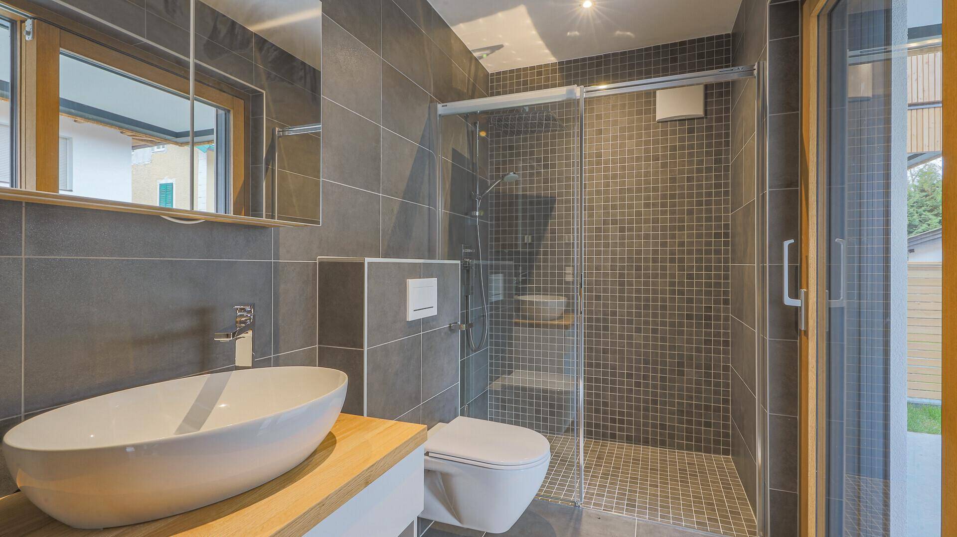 Modernes Badezimmer mit Dusche, Waschbecken und WC, ausgestattet mit grauen Fliesen.