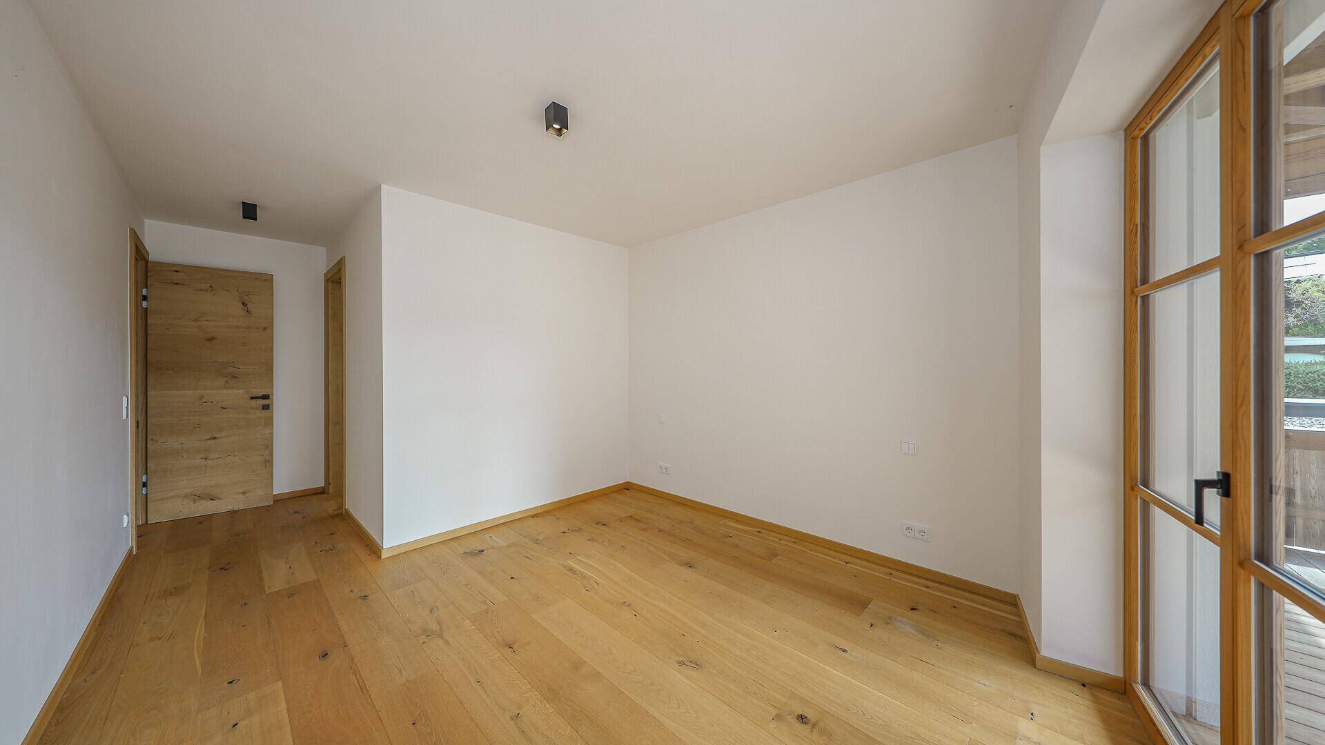 Leeres Zimmer mit hellem Holzboden und Zugang zu einem Außenbereich.