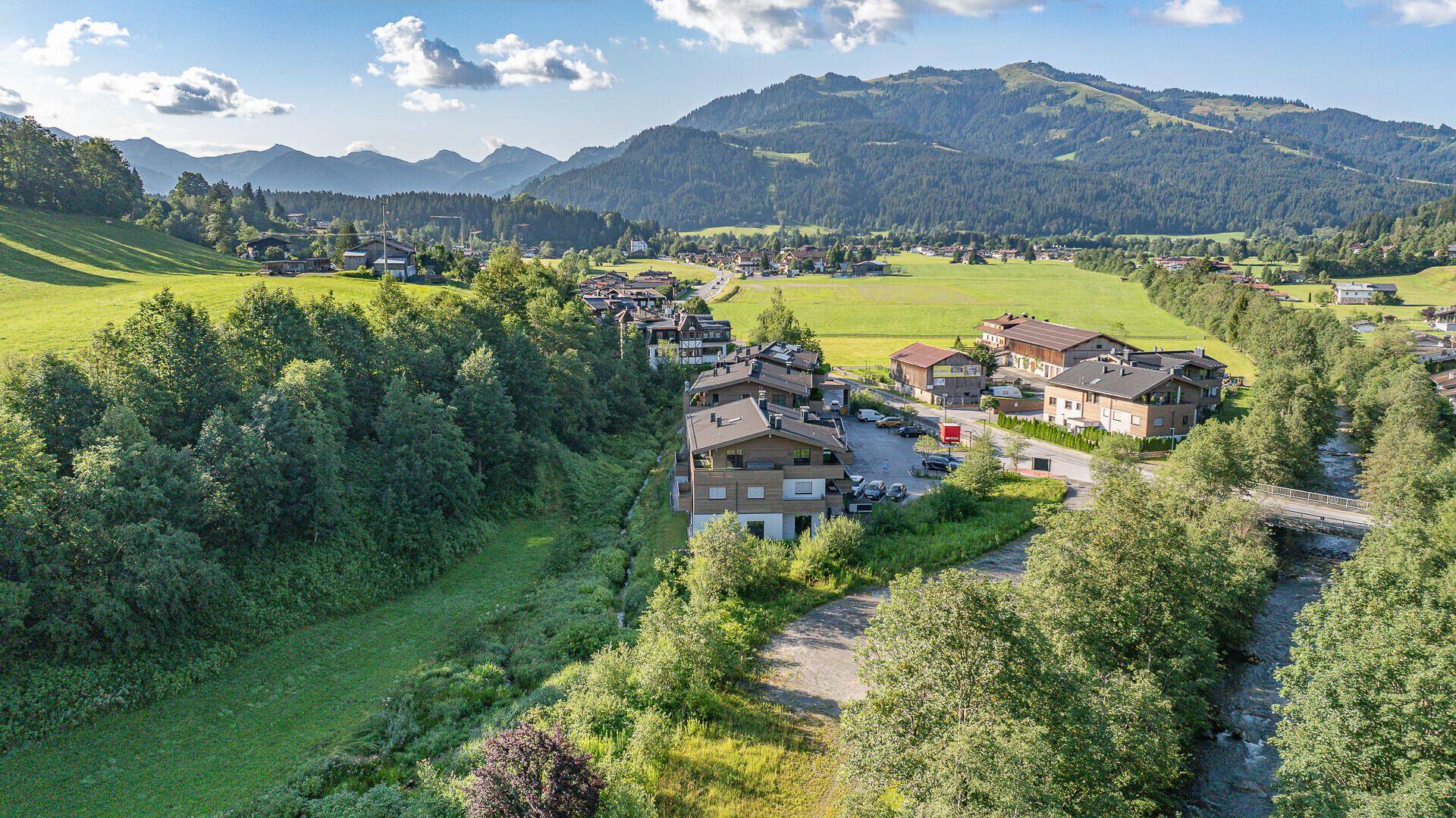 Weitläufige Luftaufnahme der ländlichen Umgebung mit Fluss, Häusern und fernen Bergen.