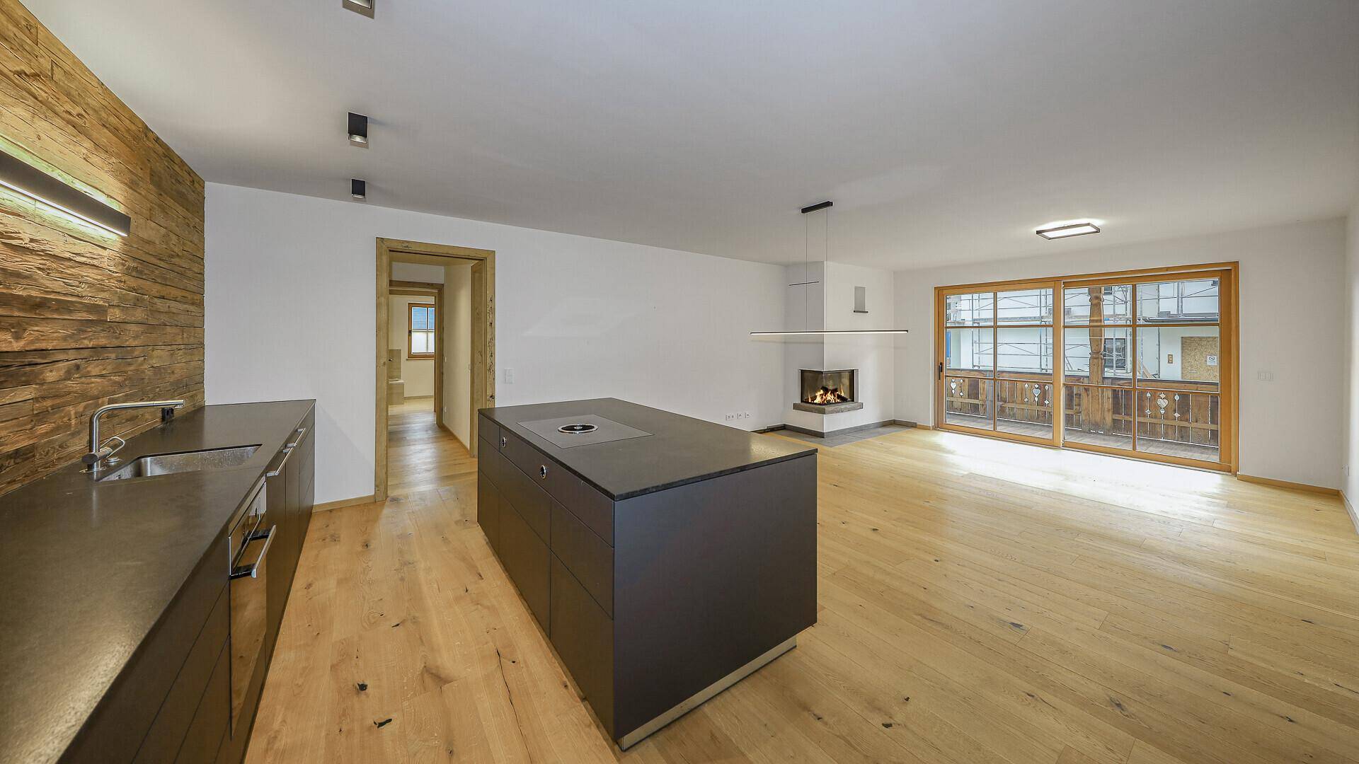 Heller offener Wohnbereich mit Holzboden, Kamin und moderner Kücheninsel.