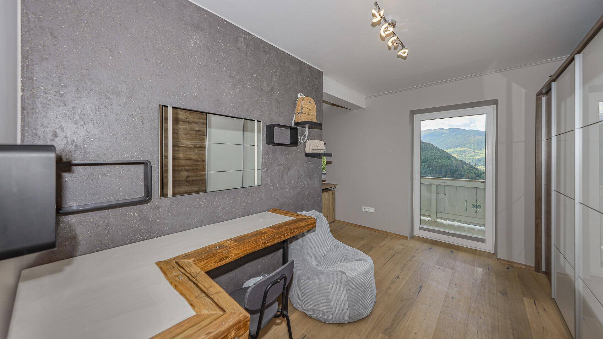 Schlafzimmer mit Holzboden, moderner Wandgestaltung und Zugang zum Balkon mit Bergblick.