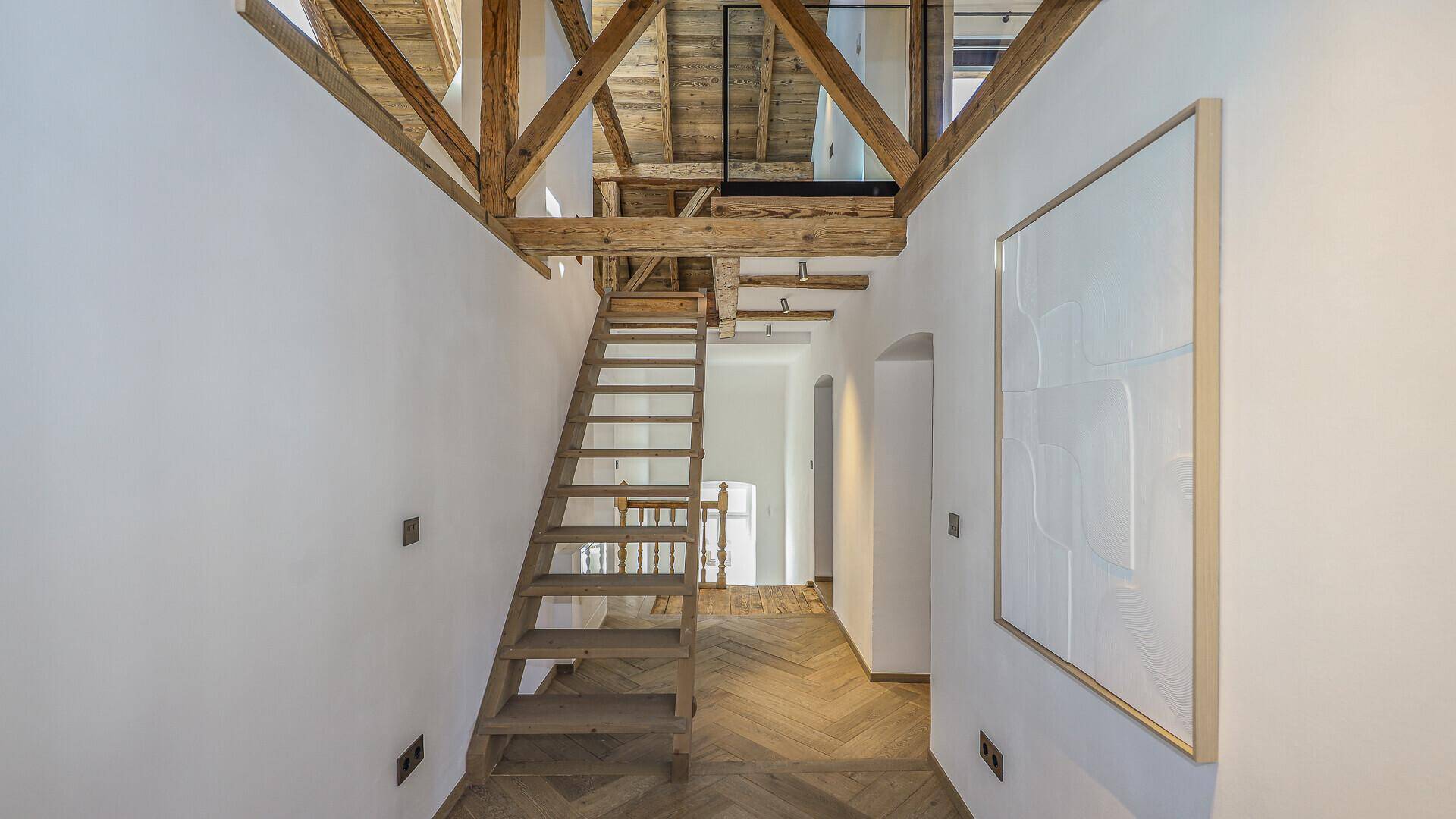 Heller Flur mit Holztreppe, die zu einer oberen Ebene führt, und sichtbaren Balken.
