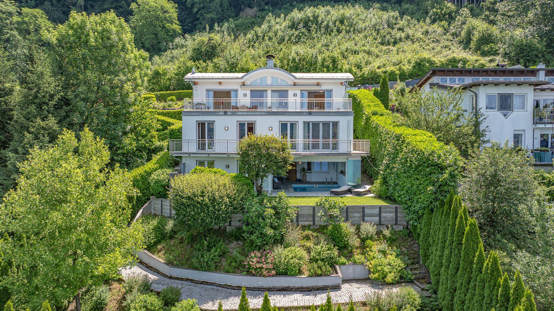 Weitläufige Ansicht der modernen Villa am Hang mit Terrassen, Balkonen und einem Poolbereich.