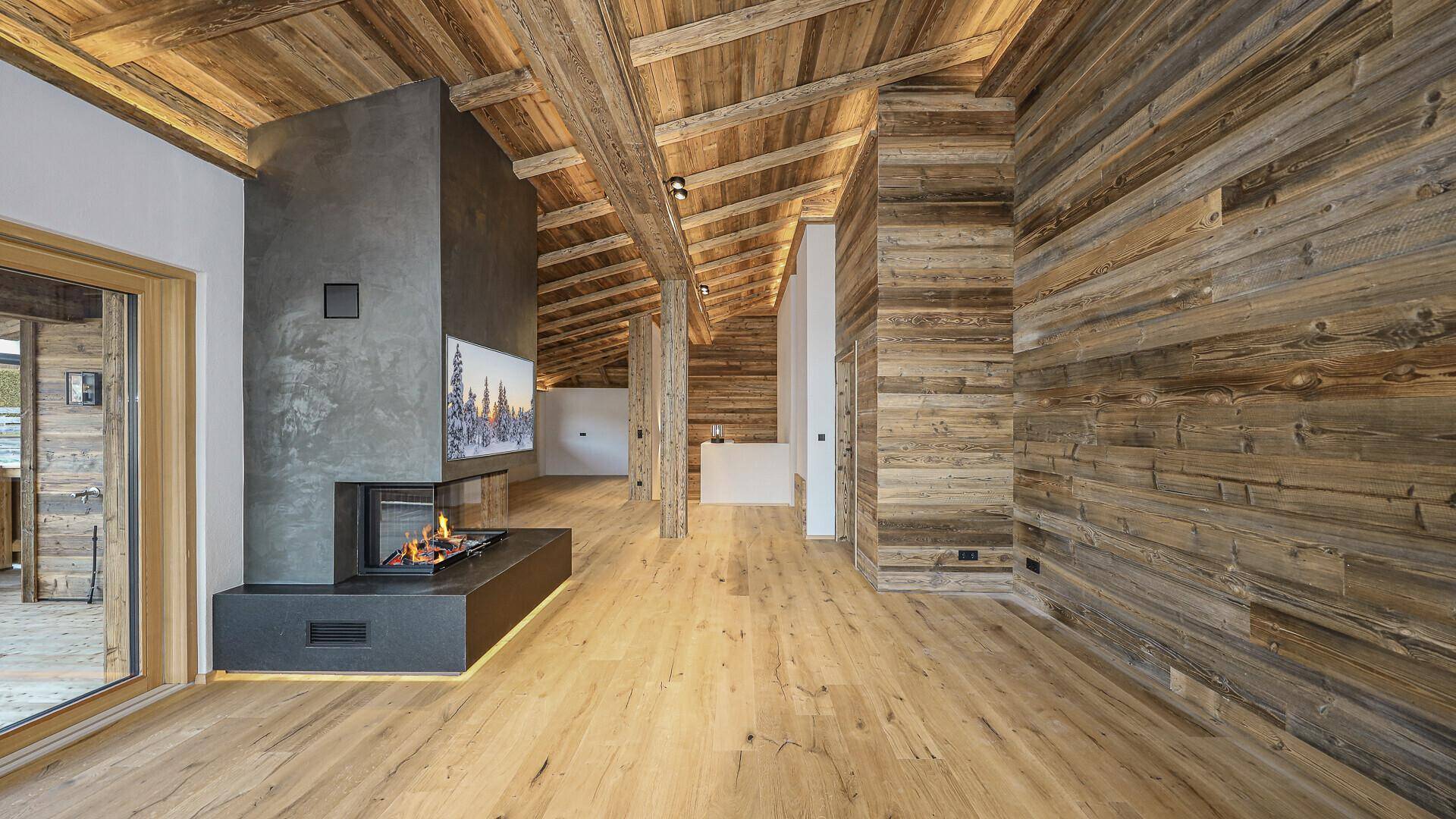 Offener Wohnbereich mit rustikalem Holzdesign, modernem Kamin und indirekter Beleuchtung.