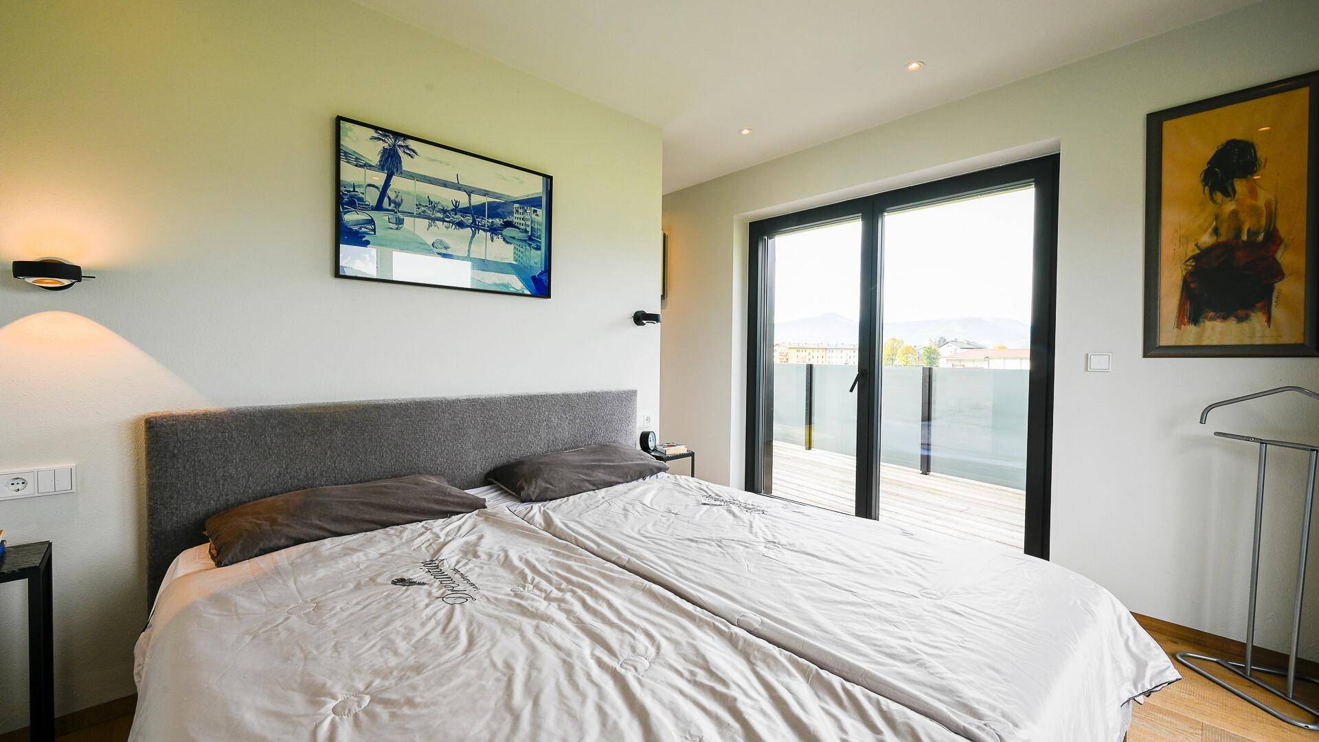 Schlafzimmer mit Doppelbett, Holzboden und Schiebetüren, die zu einer Terrasse führen.
