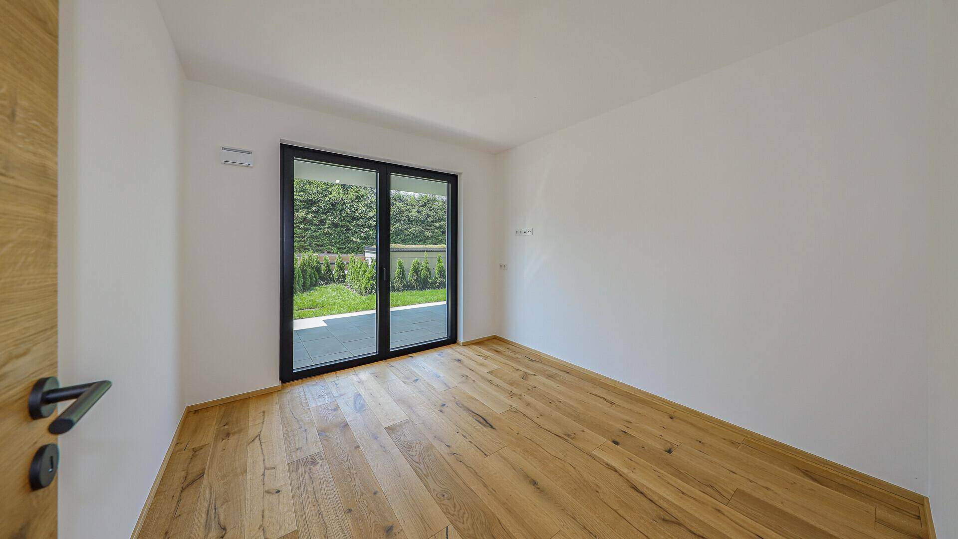 Heller, unmöblierter Raum mit Holzboden und Zugang zur Terrasse mit Bergblick.