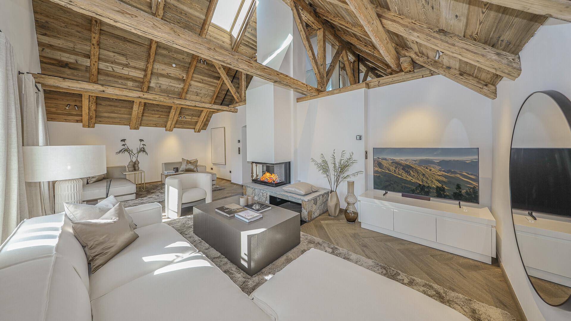 Großzügiges Wohnzimmer mit hohen Holzdecken, modernem Kamin und Blick auf die Berge.