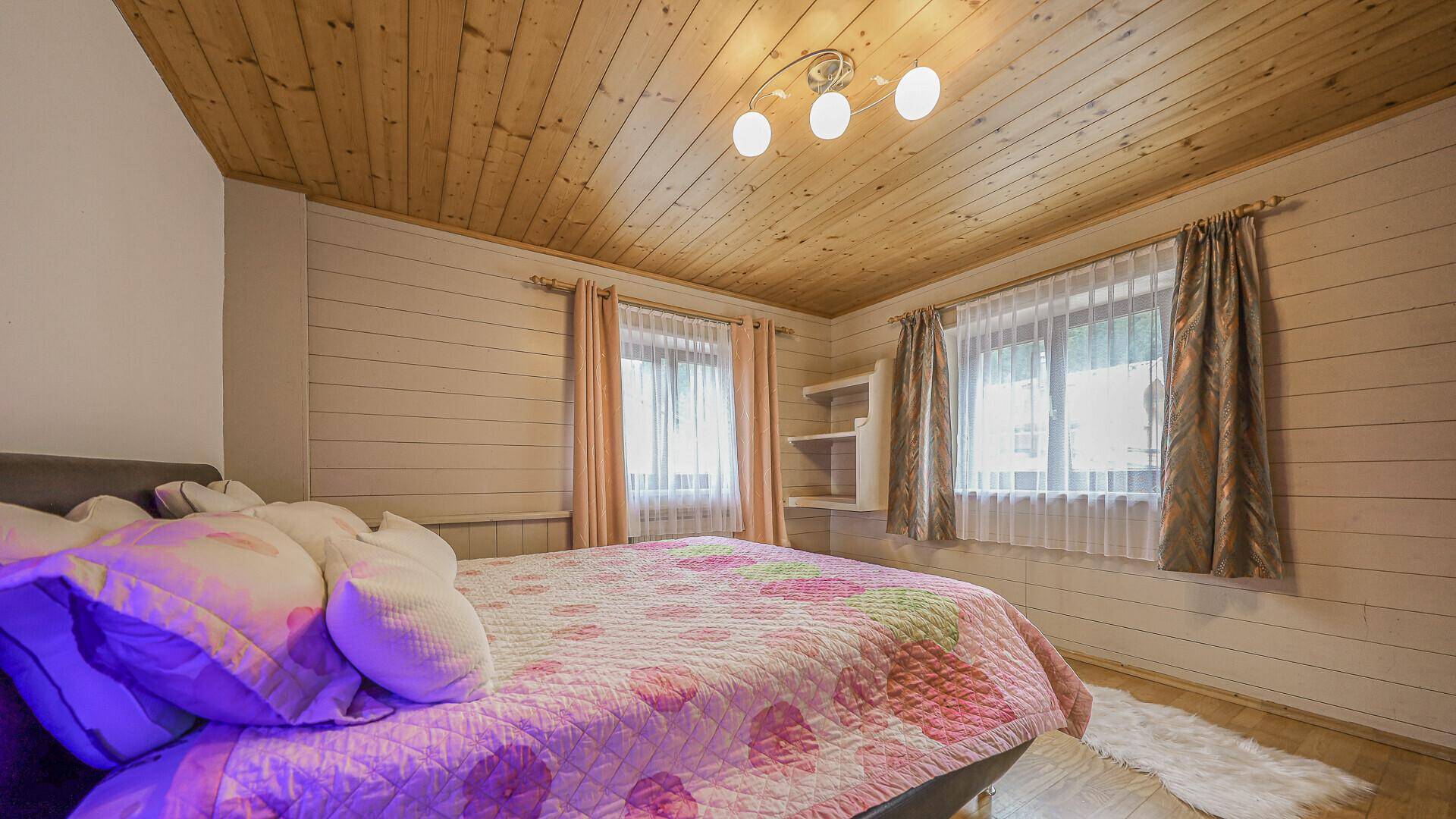 Helles Schlafzimmer mit Holzwandverkleidung und Doppelbett, ausgestattet mit bunten Kissen.