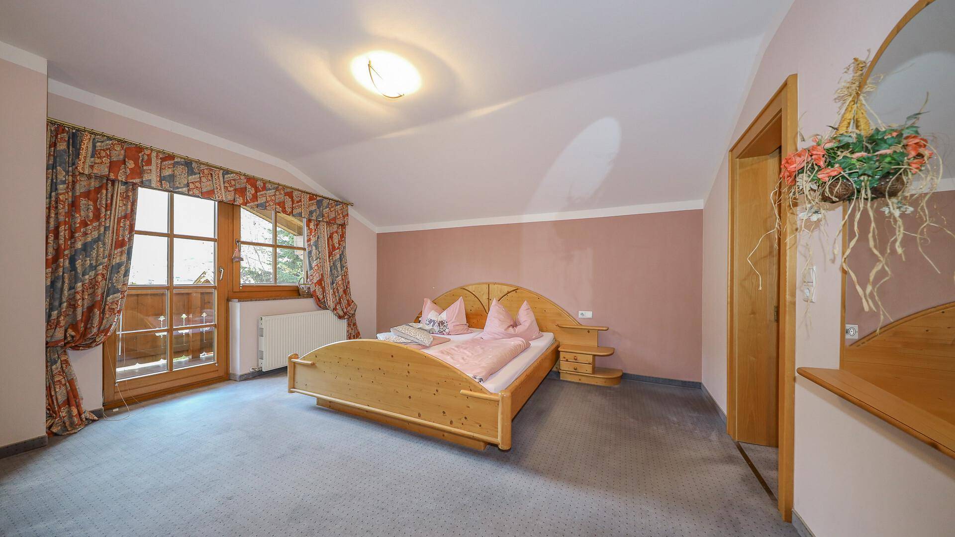 Gemütliches Schlafzimmer mit Holzbett, Teppichboden und Zugang zu einem Balkon.