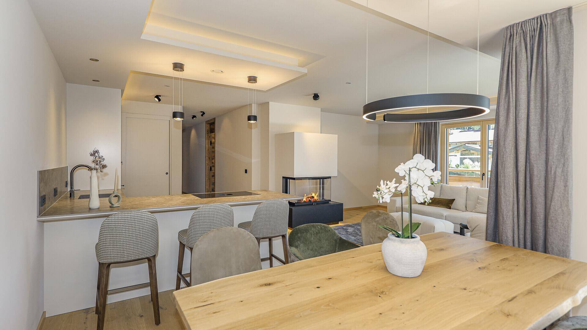 Moderne Küche mit Kochinsel und Essbereich, ausgestattet mit hochwertigen Geräten und Holztisch.