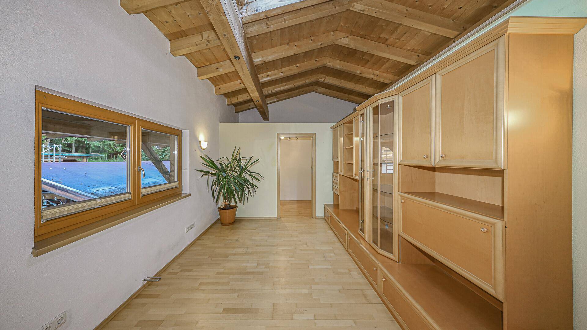 Geräumiger Innenraum mit sichtbaren Holzbalken, Holzfußboden und einem langen Einbauschrank.