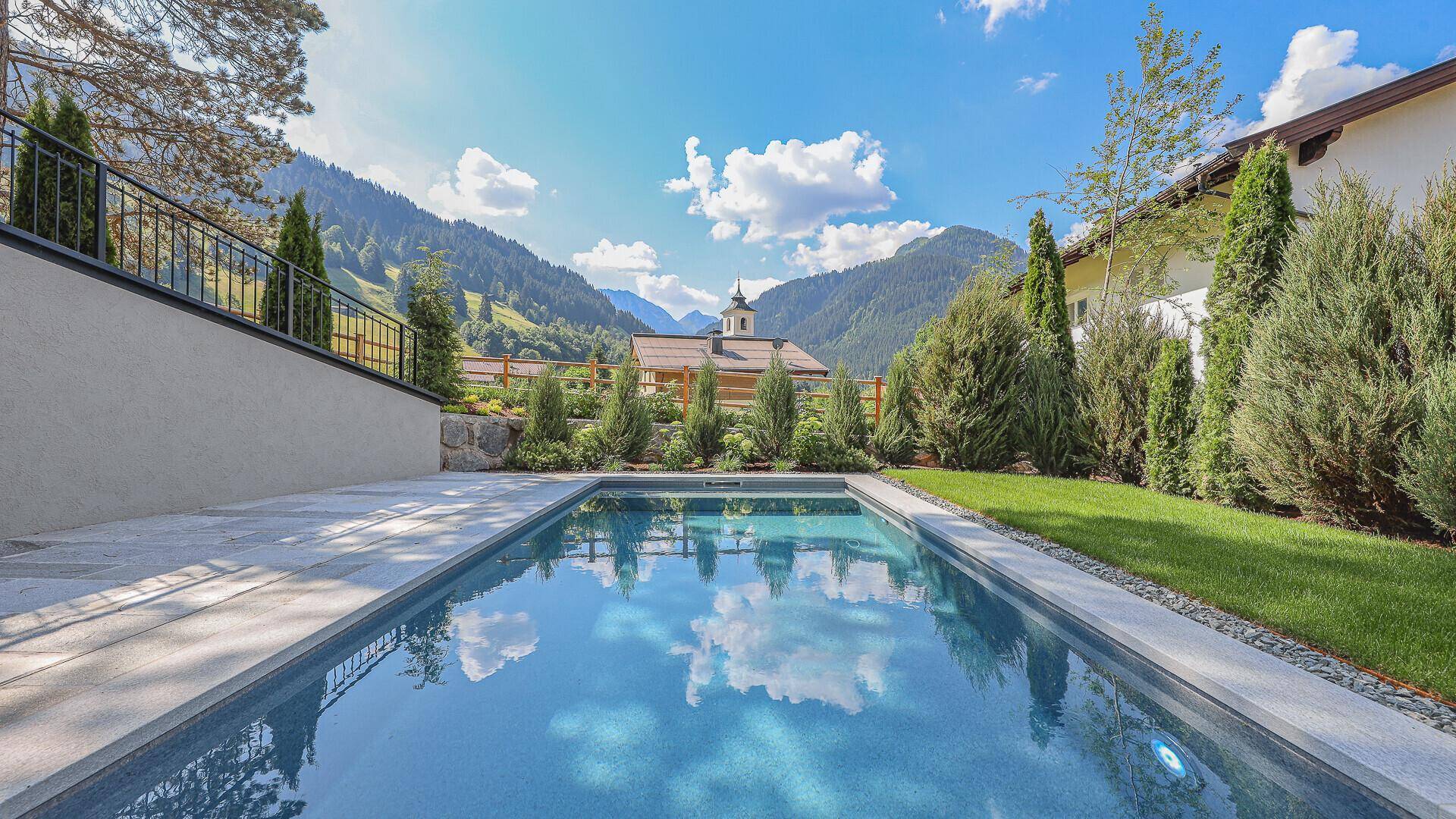 Außenpool mit gepflasterter Terrasse und weitem Blick auf die umliegende Berglandschaft.