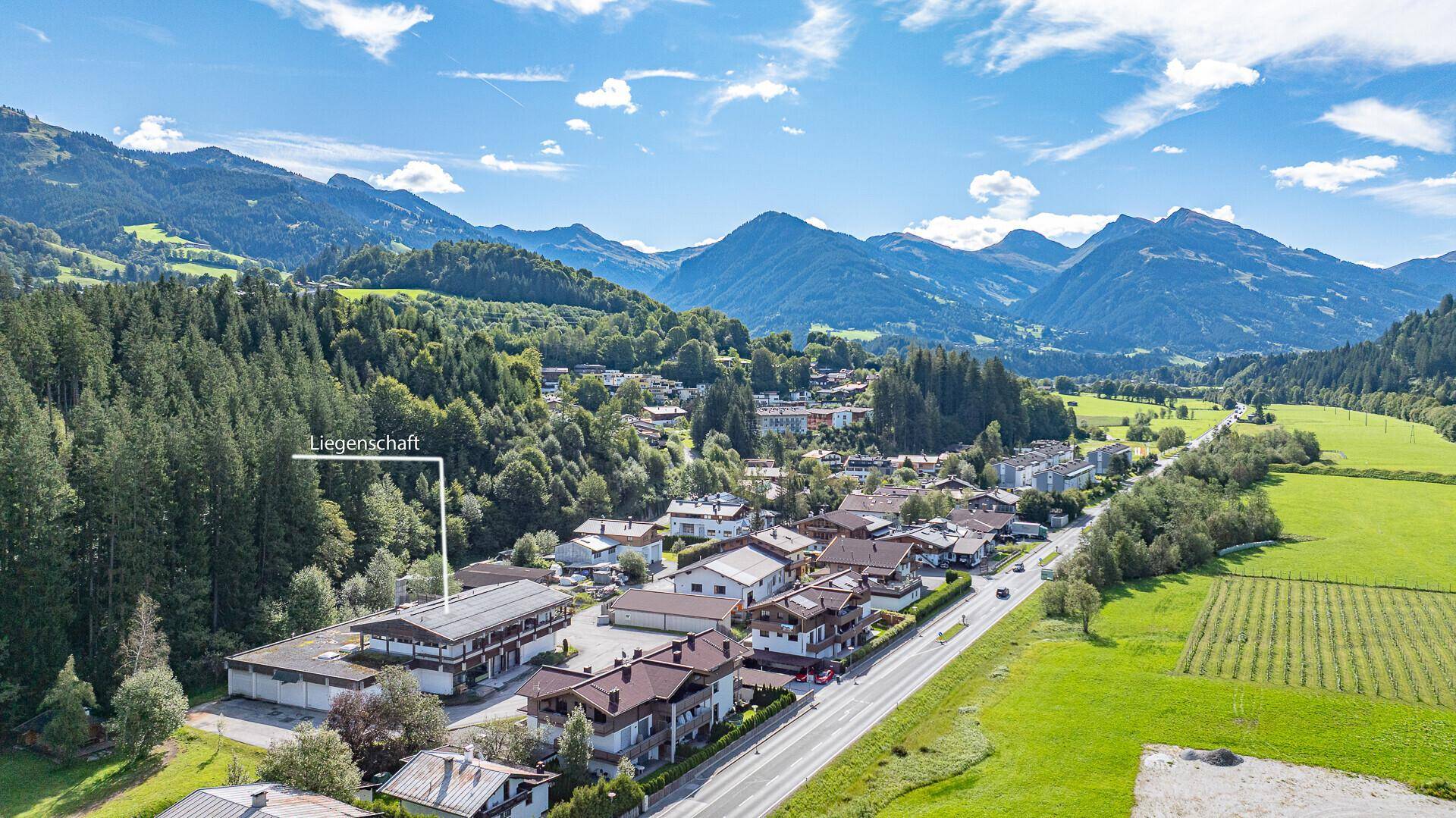 Luftaufnahme des Grundstücks in einer malerischen Berglandschaft mit Wald und angrenzender Straße.
