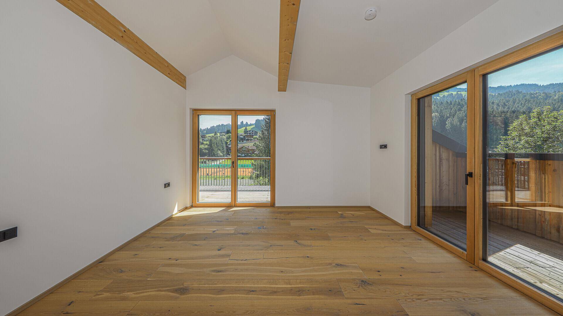 Heller Raum mit Holzboden, Dachschräge und Zugang zu einem Balkon mit Bergblick.