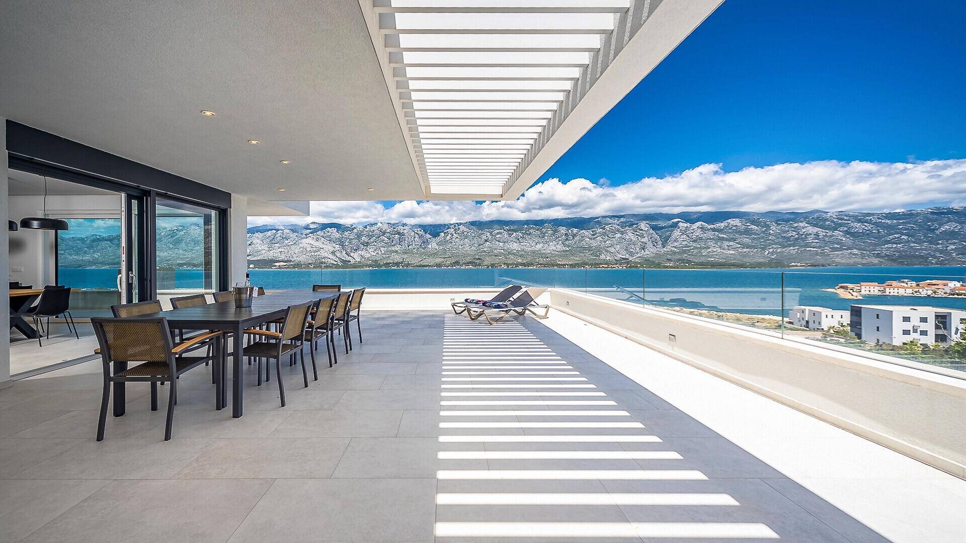 Große überdachte Terrasse im Obergeschoss mit Esstisch, Sonnenliegen und spektakulärem Meer- und Bergblick.