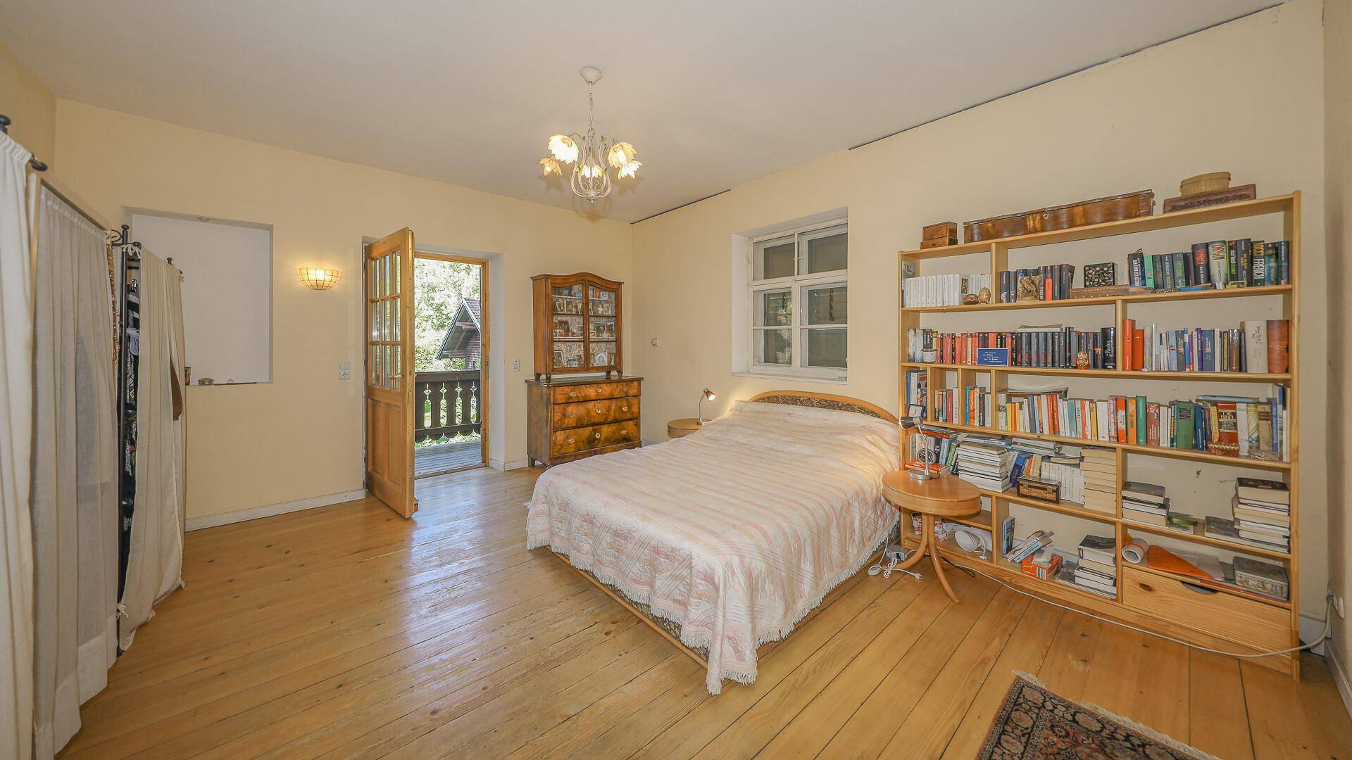 Helles Schlafzimmer mit Holzboden, Bücherregal und direktem Zugang zum Balkon.