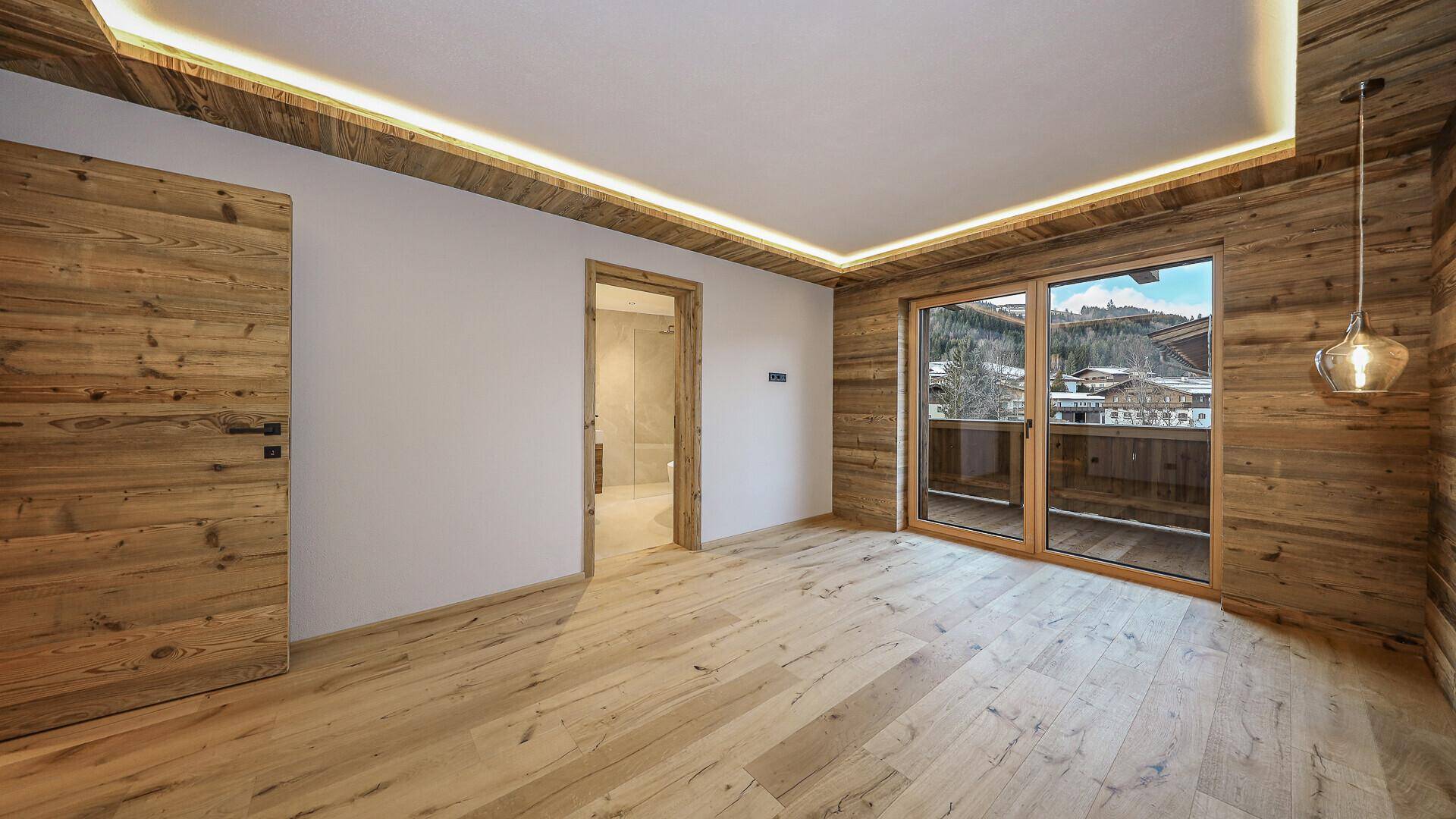 Helles Schlafzimmer mit Holzwand, Holzboden und Zugang zu einem Balkon mit Bergblick.