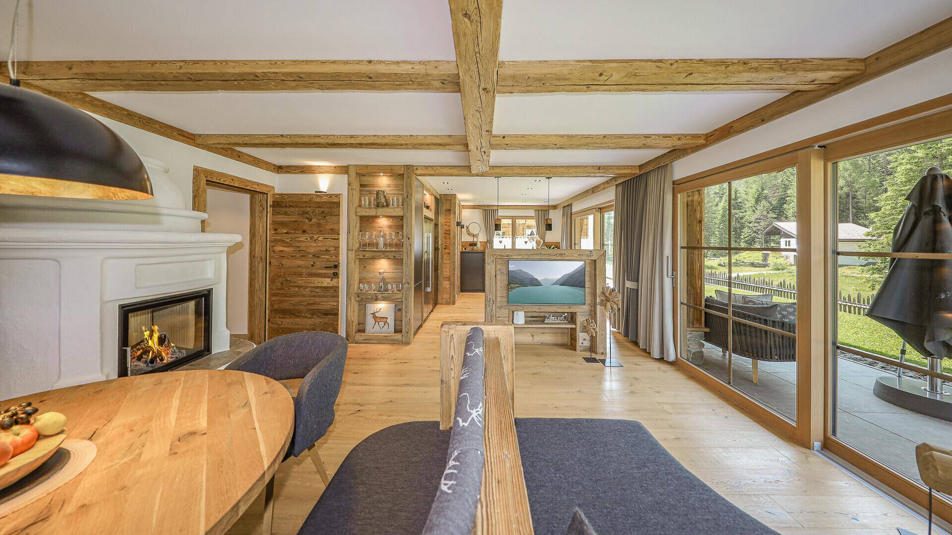 Geräumiger Wohnbereich mit Holzbalkendecke, Kamin und großen Fenstern mit Blick ins Grüne.