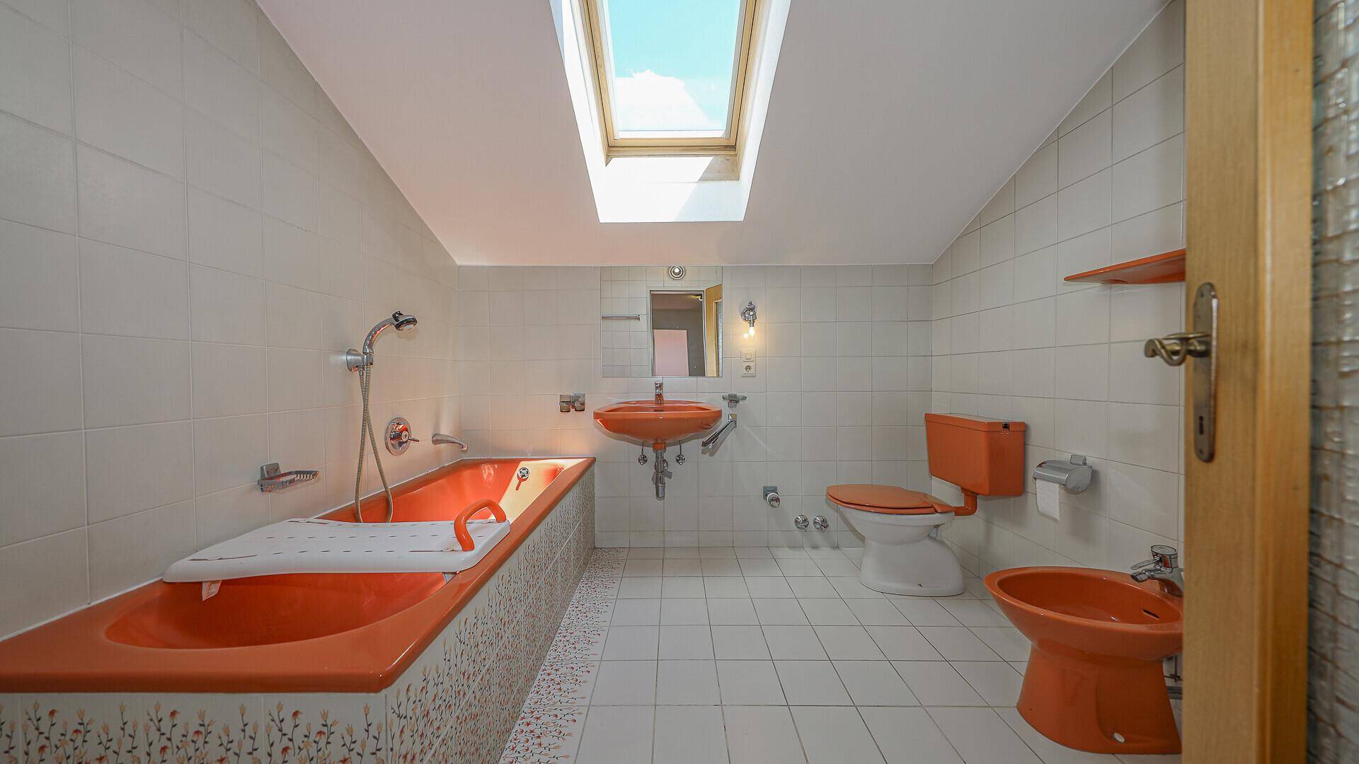 Badezimmer mit orangefarbenen Sanitärobjekten, Badewanne, Bidet und Dachfenster.
