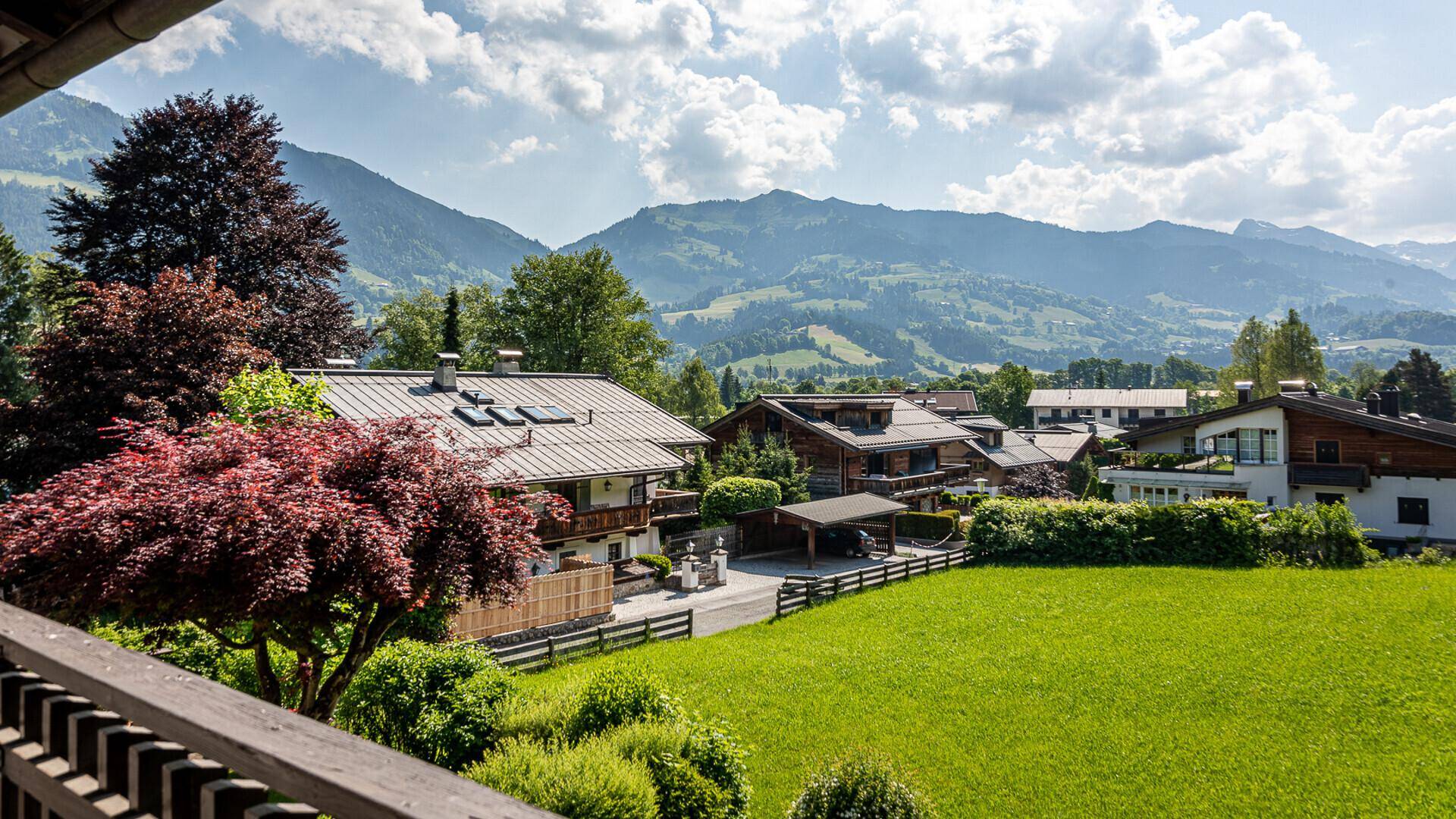 Panoramablick auf traditionelle Häuser in einer ländlichen Umgebung mit majestätischen Bergen im Hintergrund.