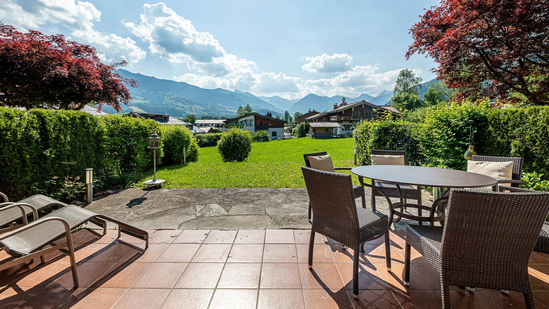 Sonnenterrasse mit Gartenmöbeln, Rasenfläche und weitem Blick auf die umliegende Berglandschaft.